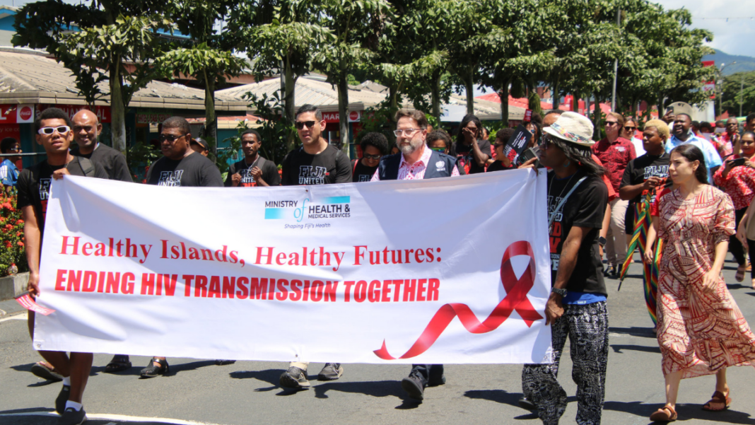 Image: Dr Mark Jacobs, WHO Director of Pacific Technical Support and WHO Representative to the South Pacific, wearing WHO vest, demonstrating alongside community members and activists on World AIDS Day (Source: WHO)